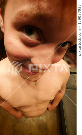 Young boy poses playfully indoors while showing his bare upper body at home Young boy poses playfully indoors while showing his bare upper body at home 139087983