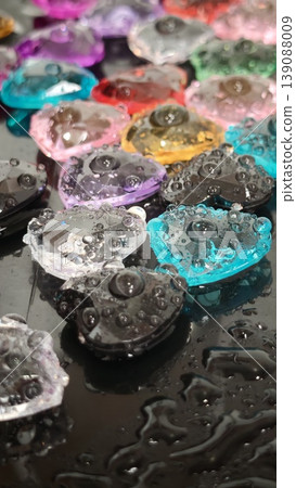 Colorful heart-shaped objects with water droplets on a black surface 139088009