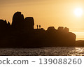 Silhouette of rocky coastline with people walking during dramatic golden sunset over calm sea 139088260