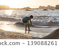 Child playing at shoreline with small waves during golden sunset light on sandy beach 139088261