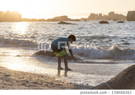 Child playing at shoreline with small waves during golden sunset light on sandy beach Child playing at shoreline with small waves during golden sunset light on sandy beach 139088261