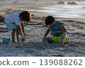 Two children playing with colorful sand toys on beach during warm sunset by ocean shore 139088262