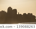 Rocky coastline silhouette at sunset with warm tones and calm sea creating peaceful horizon view 139088263