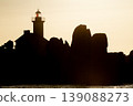 Lighthouse silhouette against golden sunset with rocky coastline creating dramatic scenic seascape composition 139088273
