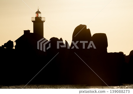 Lighthouse silhouette against golden sunset with rocky coastline creating dramatic scenic seascape composition 139088273