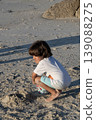 Child squatting on sandy beach playing and exploring textures during peaceful seaside afternoon 139088275