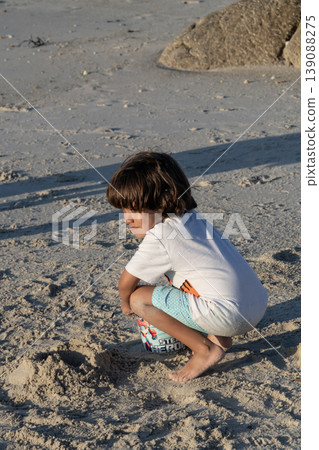 Child squatting on sandy beach playing and exploring textures during peaceful seaside afternoon Child squatting on sandy beach playing and exploring textures during peaceful seaside afternoon 139088275