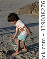 Young child playing with sand on beach bending down near rocks during warm sunny day 139088276