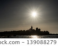 Sunset silhouette of lighthouse and rocky coastline with bright sun reflecting over calm sea 139088279