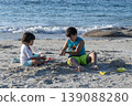 Two children playing with sand on beach near ocean waves enjoying summer seaside day 139088280