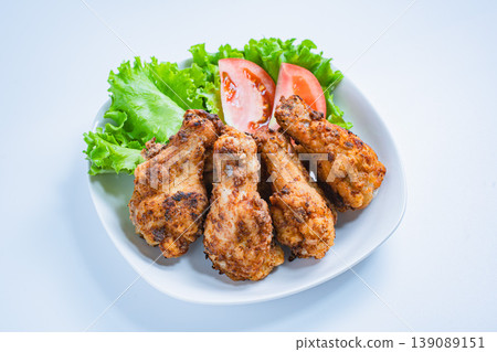 Deep-fried chicken wings with lettuce and tomato as a side dish, served on a white plate – a home-style meal. Deep-fried chicken wings with lettuce and tomato as a side dish, served on a white plate – a home-style meal. 139089151