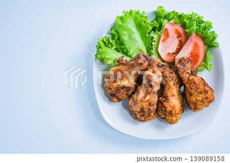 Deep-fried chicken wings with lettuce and tomato as a side dish, served on a white plate – a home-style meal. Deep-fried chicken wings with lettuce and tomato as a side dish, served on a white plate – a home-style meal. 139089158