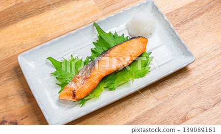鹽烤鮭魚配上磨碎的白蘿蔔:一道經典的日式烤魚料理,盛放在長長的白色盤子裡。 鹽烤鮭魚配上磨碎的白蘿蔔:一道經典的日式烤魚料理,盛放在長長的白色盤子裡。 139089161