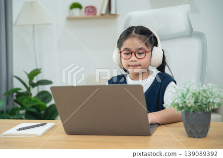 Young girl with headphones focused on laptop in modern home office, engaging in online learning or digital activities, educational technology concept Young girl with headphones focused on laptop in modern home office, engaging in online learning or digital activities, educational technology concept 139089392