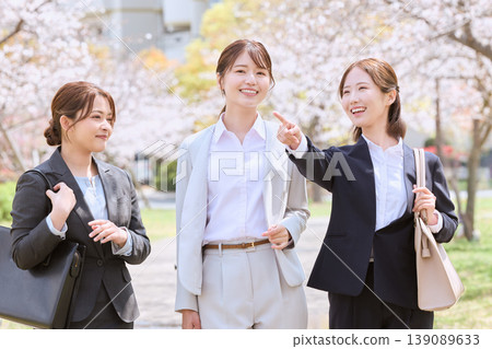 Three women in business suits smiling and chatting under a row of cherry trees – an image of spring job hunting. Three women in business suits smiling and chatting under a row of cherry trees – an image of spring job hunting. 139089633