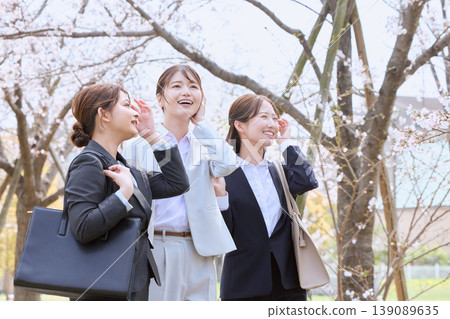 Three young female new employees walking under a row of cherry trees - a spring freshers image - businesswomen in suits Three young female new employees walking under a row of cherry trees - a spring freshers image - businesswomen in suits 139089635