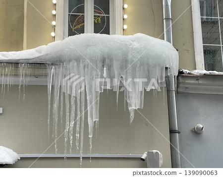 Icicles hanging from snow-covered roof of building against window Icicles hanging from snow-covered roof of building against window 139090063