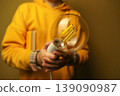 Person in yellow hoodie holding a large vintage Edison light bulb. Concept of creative idea, innovation, and inspiration. Close-up of a decorative lamp in hands with a blurred background 139090987