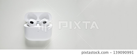 Wireless white earphones in a charging case on a light background. Minimalist composition of modern earbuds with large copy space for design. Technology and audio gadget concept 139090991