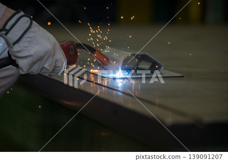 Close-up of hands working in metalworking with arc welding, where sparks fly, in a manufacturing plant. Industrial technology background material. Close-up of hands working in metalworking with arc welding, where sparks fly, in a manufacturing plant. Industrial technology background material. 139091207