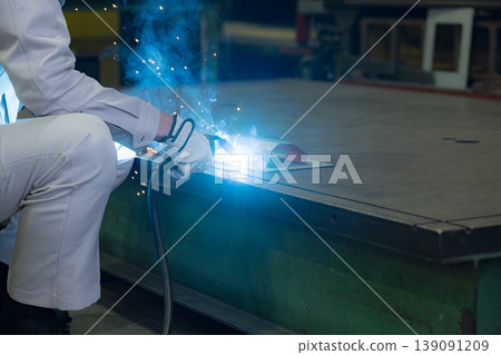 Close-up of hands working in metalworking with arc welding, where sparks fly, in a manufacturing plant. Industrial technology background material. Close-up of hands working in metalworking with arc welding, where sparks fly, in a manufacturing plant. Industrial technology background material. 139091209