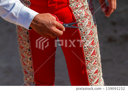 Close up detail of a bullfighter holding scissors next to his red traje de luces during a summer bullfight. Close up detail of a bullfighter holding scissors next to his red traje de luces during a summer bullfight. 139091232