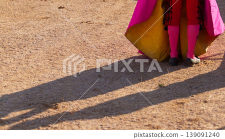 Close up of a bullfighter costume of pink stockings, black shoes, yellow and pink cape on the sand. Close up of a bullfighter costume of pink stockings, black shoes, yellow and pink cape on the sand. 139091240