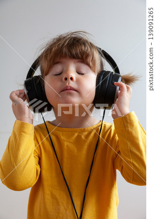 Portrait of a three year old girl with pigtails wearing yellow and listening to music with big headphones Portrait of a three year old girl with pigtails wearing yellow and listening to music with big headphones 139091265