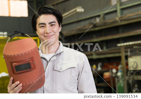 A worker wearing a welding mask – an image of a craftsman or welder at a manufacturing site. Stay safe today! A worker wearing a welding mask – an image of a craftsman or welder at a manufacturing site. Stay safe today! 139091534