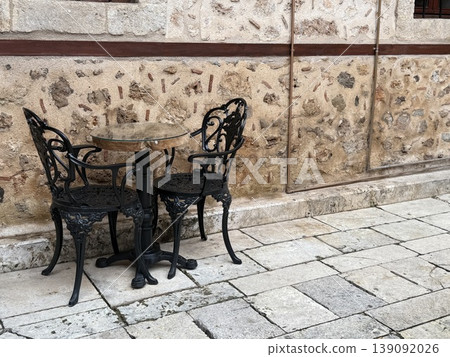 Outdoor cafe setting with antique metal chairs and stone wall background Outdoor cafe setting with antique metal chairs and stone wall background 139092026