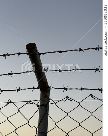 Barbed wire on metal fence with clear sky in background showing security or confinement concept Barbed wire on metal fence with clear sky in background showing security or confinement concept 139092032