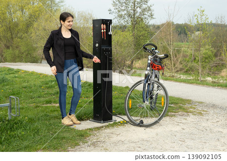 Woman inflating a bicycle tire using a manual pump station. 139092105