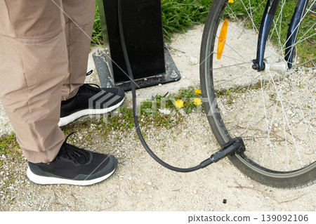 Close-up of feet and bike pump nozzle at a repair station. Close-up of feet and bike pump nozzle at a repair station. 139092106