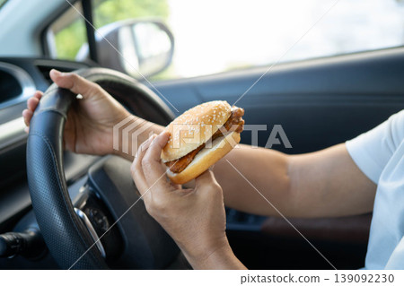 Asian woman driver hold and eat hamburger in car, dangerous and risk an accident. Asian woman driver hold and eat hamburger in car, dangerous and risk an accident. 139092230