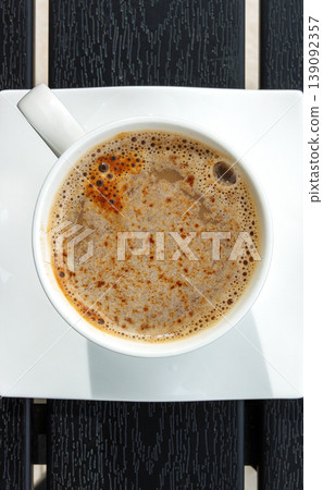 Cup of coffee on a square white saucer, placed on a dark slatted table. Selective focus. Copy space Cup of coffee on a square white saucer, placed on a dark slatted table. Selective focus. Copy space 139092357