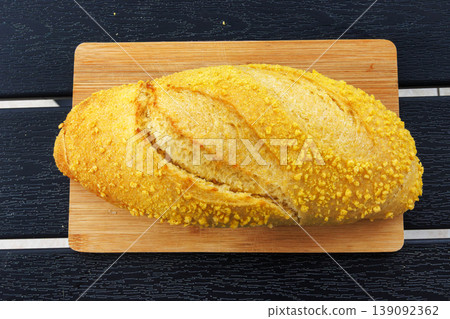 Overhead view of a croatian corn bread loaf placed on a wooden cutting board on a dark slatted table. Selective focus Overhead view of a croatian corn bread loaf placed on a wooden cutting board on a dark slatted table. Selective focus 139092362