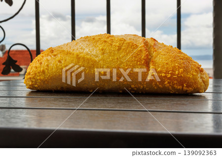 Croatian corn bread loaf on a balcony table with a view on Adriatic sea and rooftops in Makarska, Croatia in blurred background. Selective focus Croatian corn bread loaf on a balcony table with a view on Adriatic sea and rooftops in Makarska, Croatia in blurred background. Selective focus 139092363