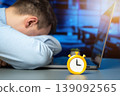 Sleeping businessman and an alarm clock while sitting in an office at a laptop. Concept of tired, deadline pressure, time management, urgency, productivity, multitasking, and work efficiency 139092565