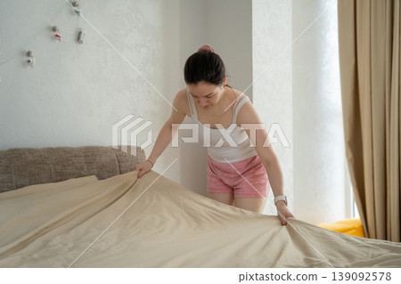 A caucasian woman made her bed in her bedroom on a sunny day. morning routine A caucasian woman made her bed in her bedroom on a sunny day. morning routine 139092578