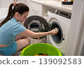 A young 31 year old brunette woman loads dirty laundry into a washing machine in the bathroom 139092583