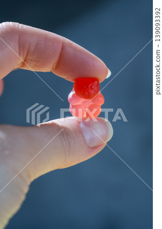 Food supplements. Female hand holding one vitamin jelly gummy bear shaped against dark background Food supplements. Female hand holding one vitamin jelly gummy bear shaped against dark background 139093392