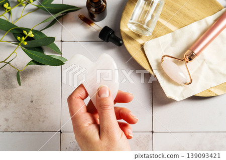 Rose quartz gua sha tool in female hand, face massage tool, beauty abstract photo Rose quartz gua sha tool in female hand, face massage tool, beauty abstract photo 139093421