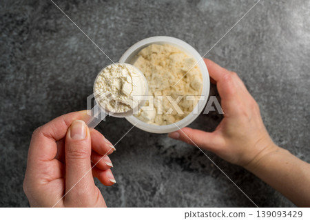 Female hands holding a scoop of protein whey powder, white plastic tube, on dark background Female hands holding a scoop of protein whey powder, white plastic tube, on dark background 139093429