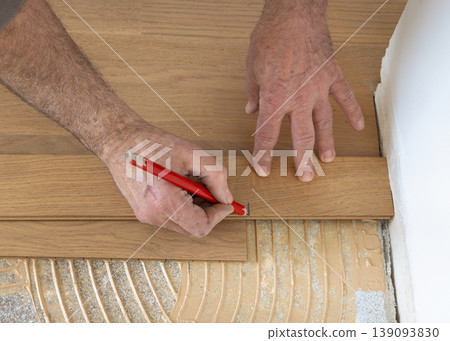 Construction worker marking parquet plank with pencil during hardwood flooring installation Construction worker marking parquet plank with pencil during hardwood flooring installation 139093830
