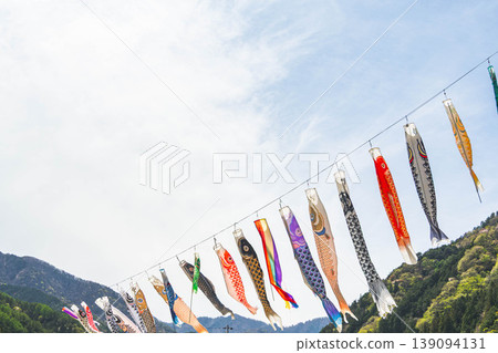 Colorful carp streamers swim against the blue sky and lush green mountains. Colorful carp streamers swim against the blue sky and lush green mountains. 139094131