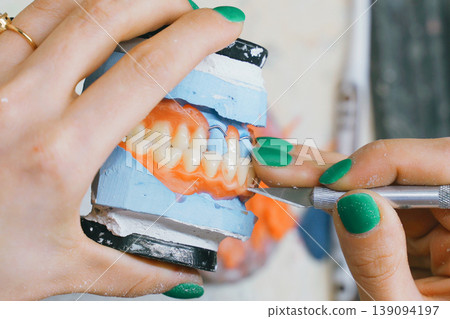 Meticulous craft of a dental technician shaping dentures in the workshop Meticulous craft of a dental technician shaping dentures in the workshop 139094197