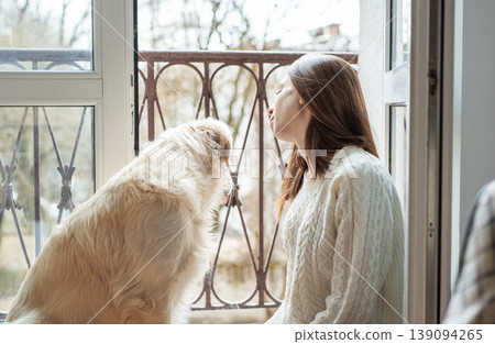 Woman and golden retriever dog looking out balcony window Woman and golden retriever dog looking out balcony window 139094265