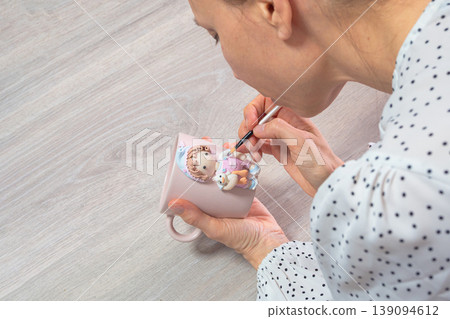 Woman paints delicate design on pink ceramic mug 139094612