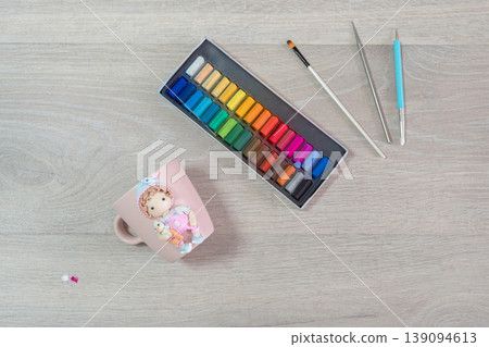 Colorful paints rest beside a ceramic mug with a child's face 139094613