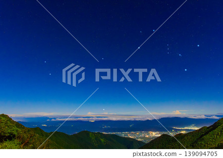 Night view from the Northern Alps: The city lights of Azumino and Matsumoto Plain and Orion rising in the night sky. 139094705